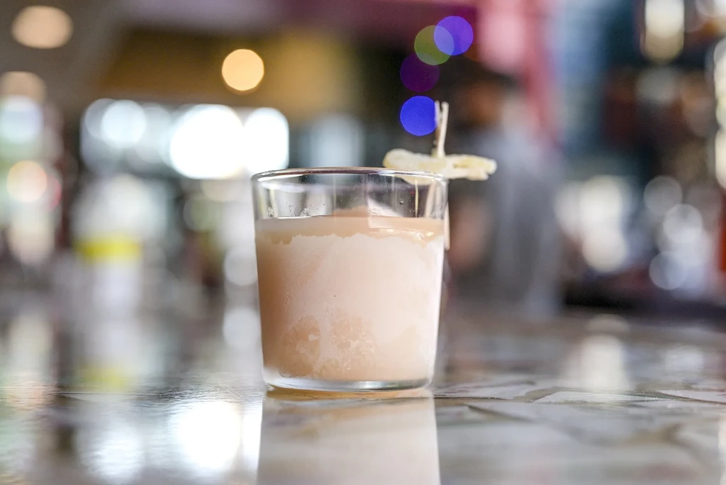 Light brown frothy drink in a frosted glass with fruit garnish.