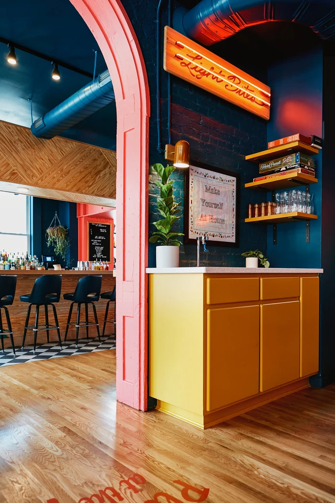 Modern bar interior with a pink archway, yellow cabinet, teal wall.