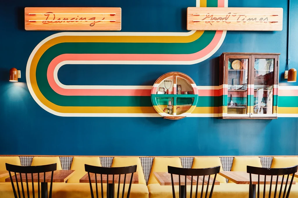 Retro restaurant interior with teal wall, striped pattern, and neon signs.