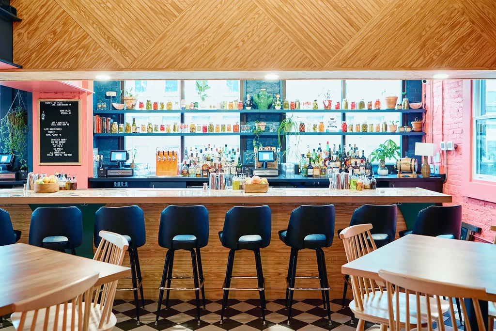 Well-stocked modern bar with black stools, pink arch, and checkered floor.
