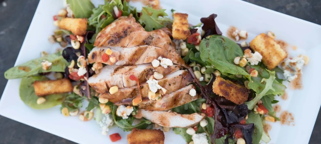 Close-up grilled chicken salad with lettuce, corn, peppers, and cheese.