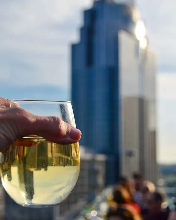 Hand holding wine glass reflecting cityscape, blurred skyscraper and people.