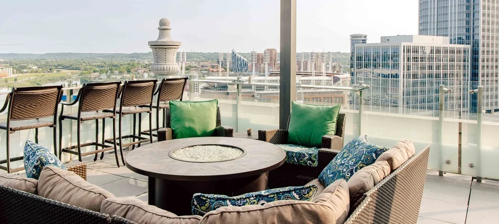 Empty rooftop patio with wicker seating, fire pit, and city view.