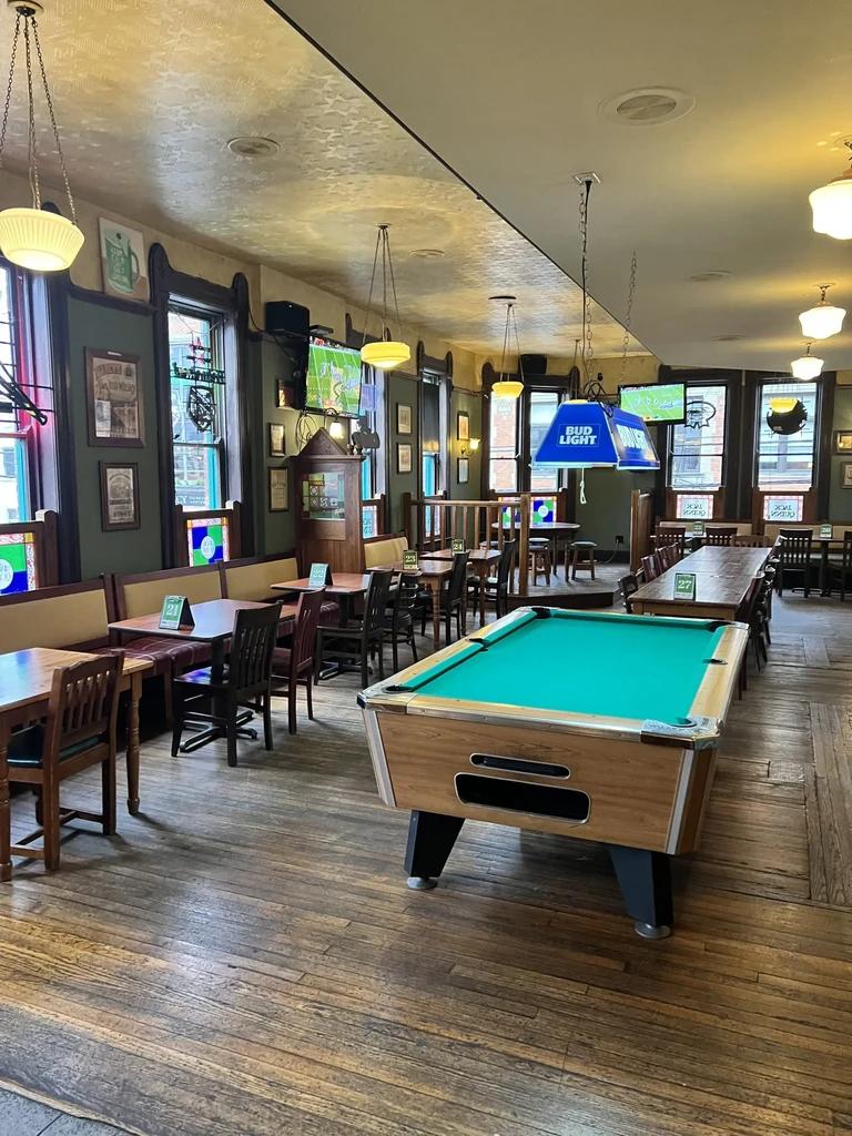 Empty rustic pub interior with green pool table and sports TVs.