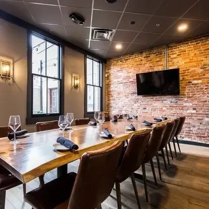 Rustic dining room with long wooden table, leather chairs, and brick wall.