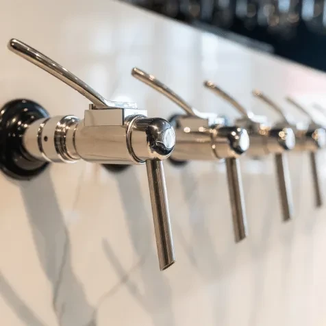 Five modern, polished metallic beverage taps on a light backsplash.