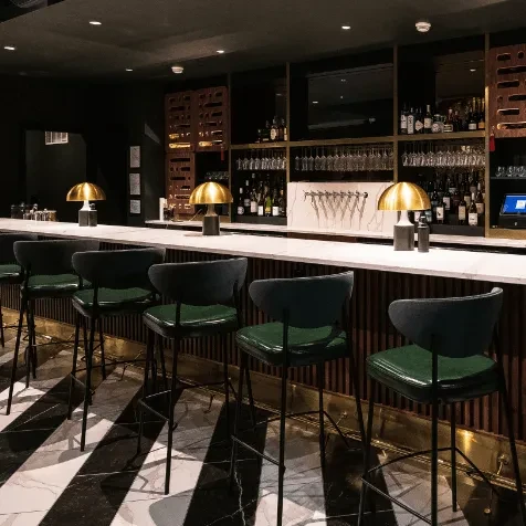 Empty modern bar with dark green stools, marble counter, and striped floor.