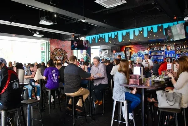 Crowded modern bar interior with people, unique murals, and blue lighting.