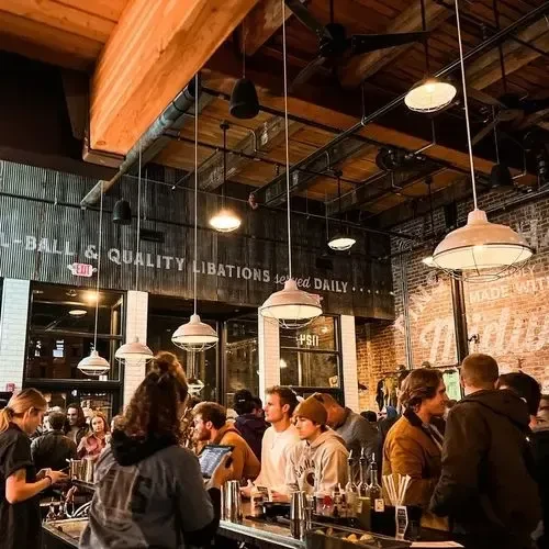 Bustling industrial-chic bar with exposed beams and many patrons.