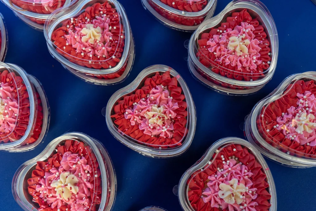 Multiple heart-shaped cakes with red, pink, cream floral frosting and sprinkles.