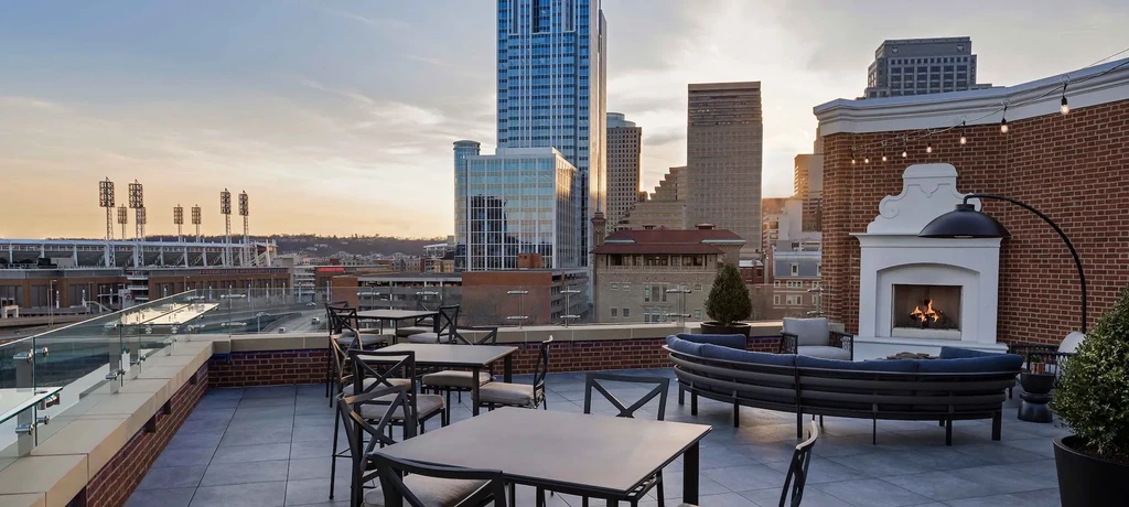 Modern rooftop patio with varied seating, outdoor fireplace, and sunset cityscape.