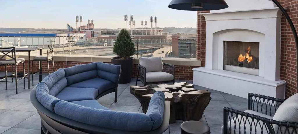 Modern rooftop patio with fireplace, stylish seating, and city stadium view.