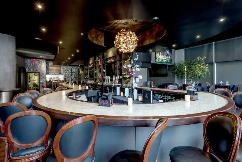 Modern horseshoe-shaped bar in restaurant, with stools and ornate chandelier.