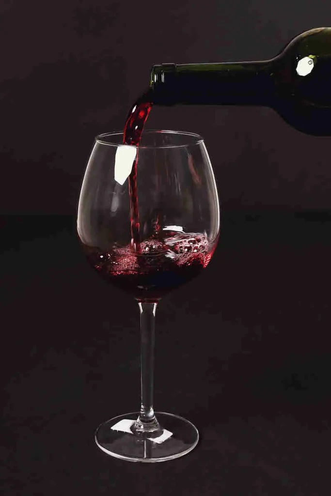 Dark bottle pours red wine into a glass, creating a splash.
