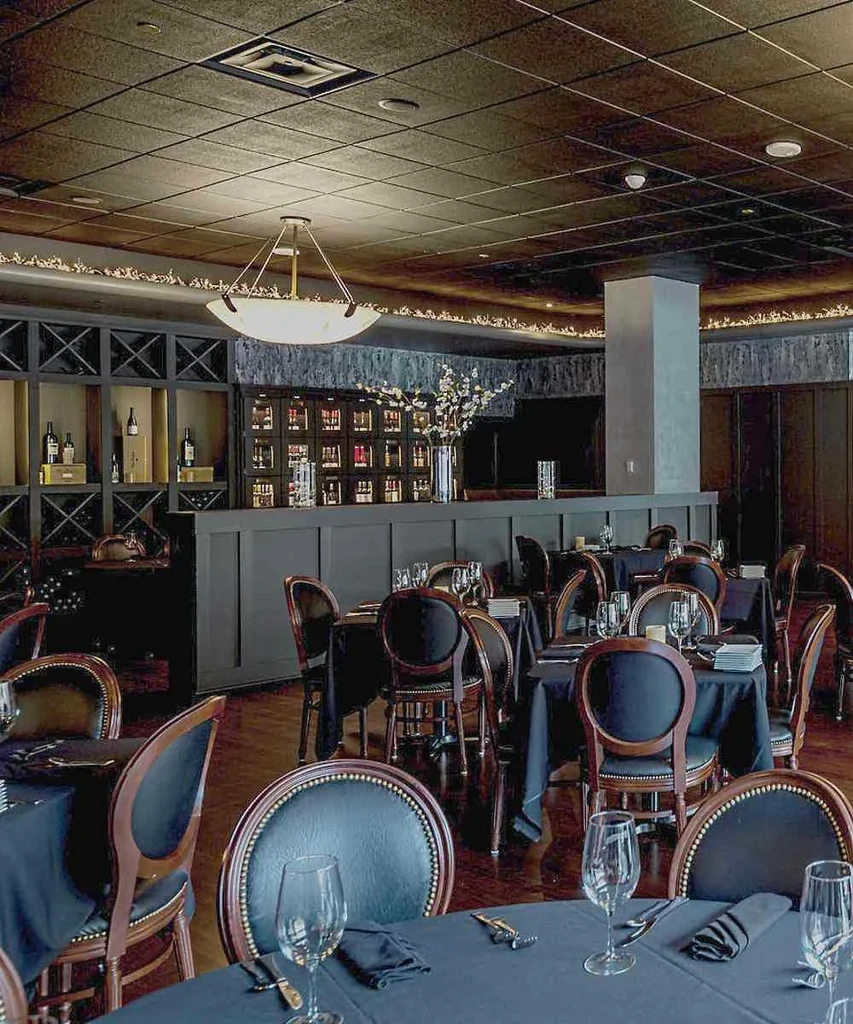 Elegant restaurant interior with dark tables, bar, and prominent chandelier.
