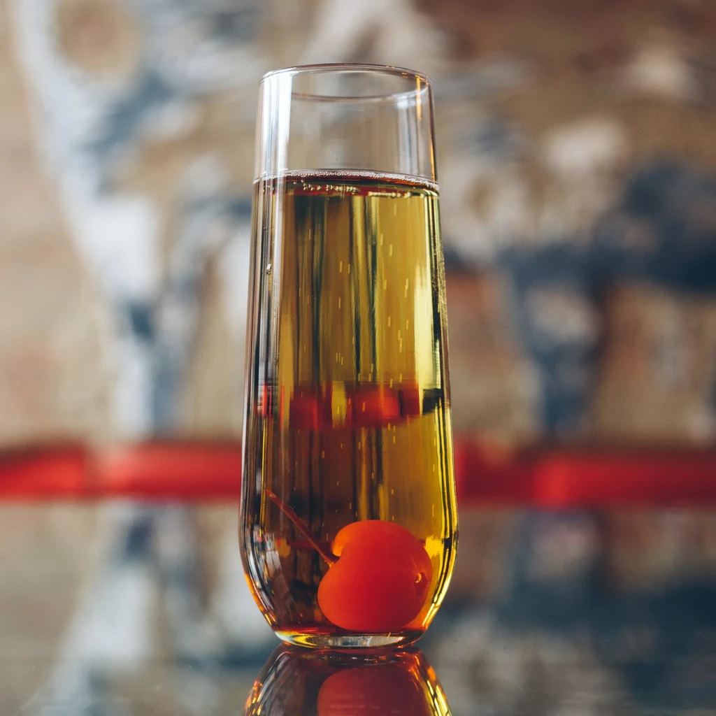 Golden sparkling drink in a stemmed glass with a red cherry garnish.