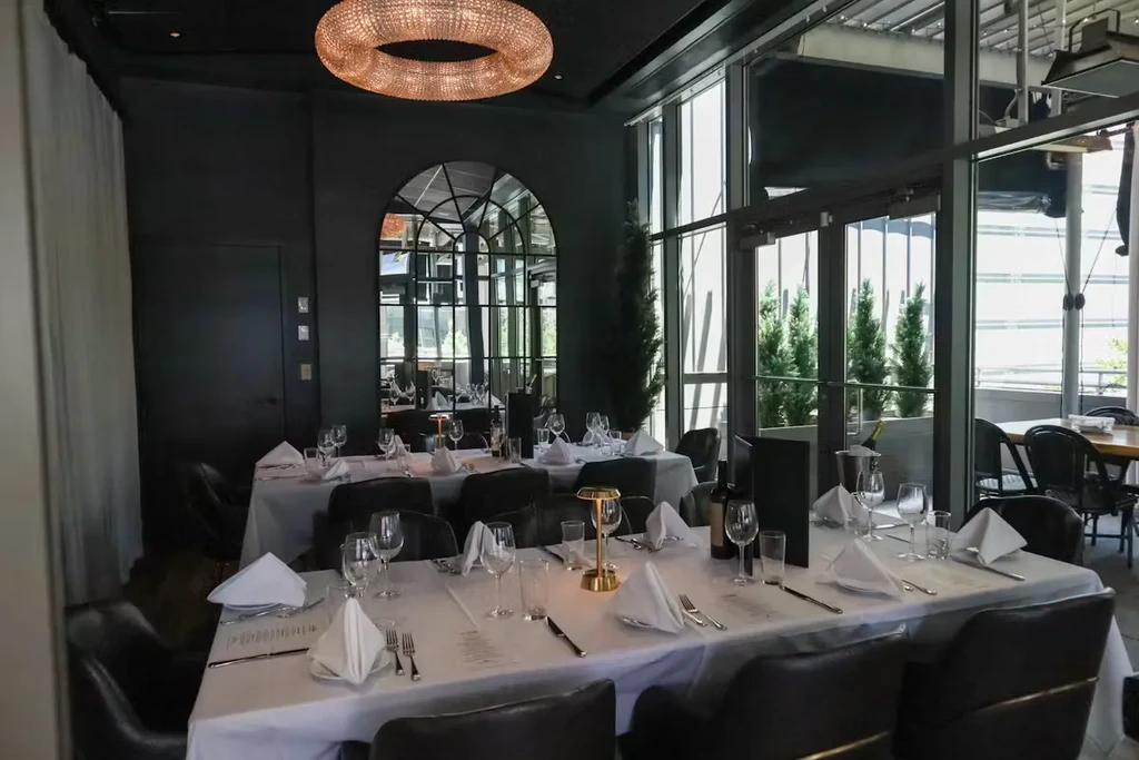 Sophisticated restaurant dining room with set tables and outdoor plants.