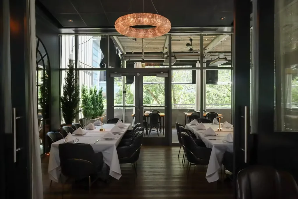 Restaurant dining room with set tables, ornate chandelier, and outdoor patio view.