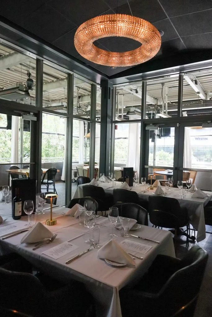 Empty restaurant interior with set tables, ornate chandelier, and patio view.