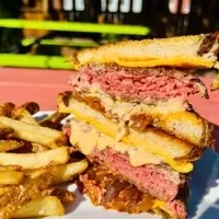 Patty melt cut in half, showing beef patties, melted cheese, and fries.