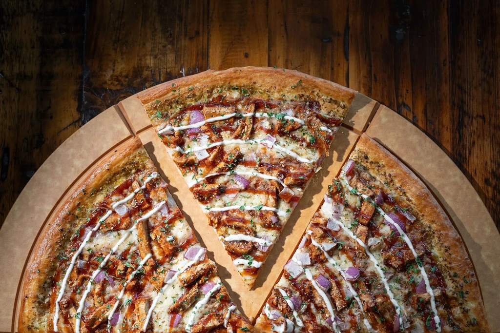 BBQ chicken pizza with onions, herbs, and two sauces, one slice pulled.