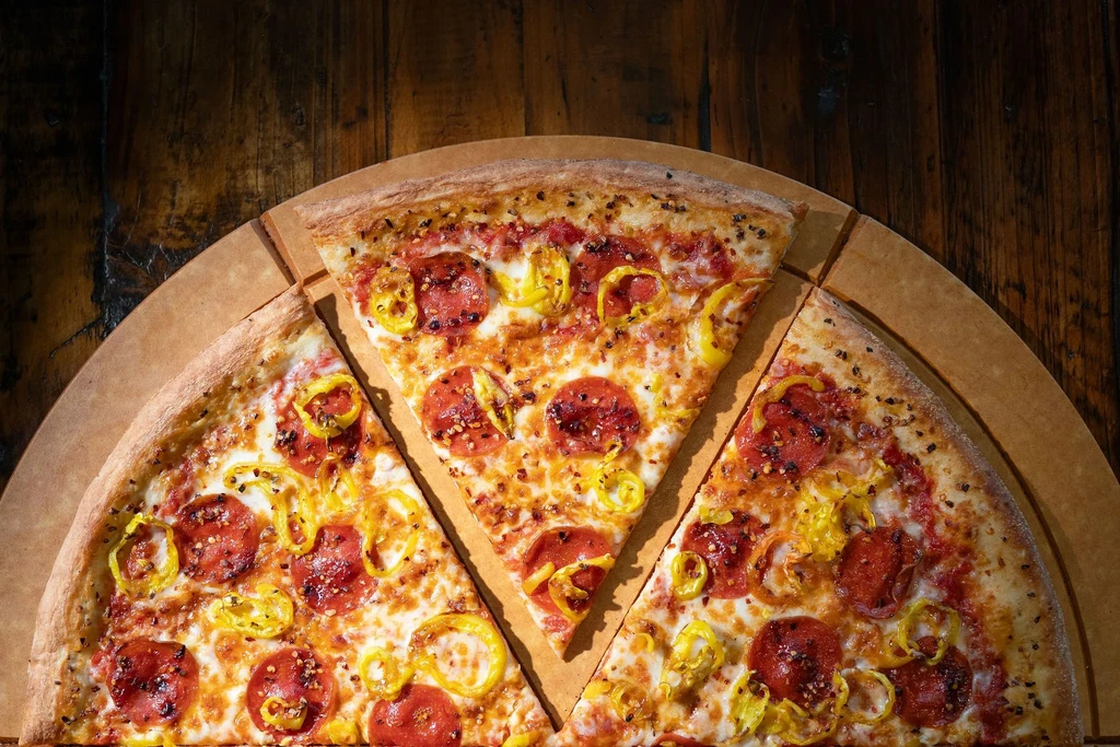 Close-up, overhead view of pepperoni and banana pepper pizza, three slices cut.