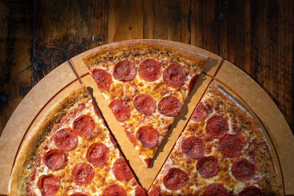 Overhead pepperoni pizza, two separated slices, on a rustic wooden table.