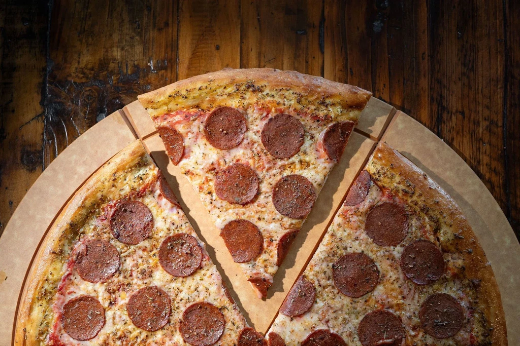 Close-up overhead of sliced pepperoni pizza, melted cheese, on rustic wood.