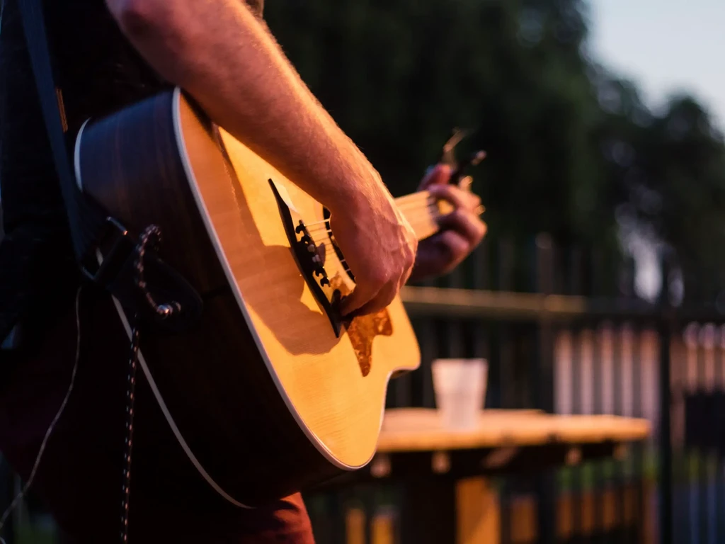 Close-up: hands playing acoustic guitar in warm outdoor evening light.