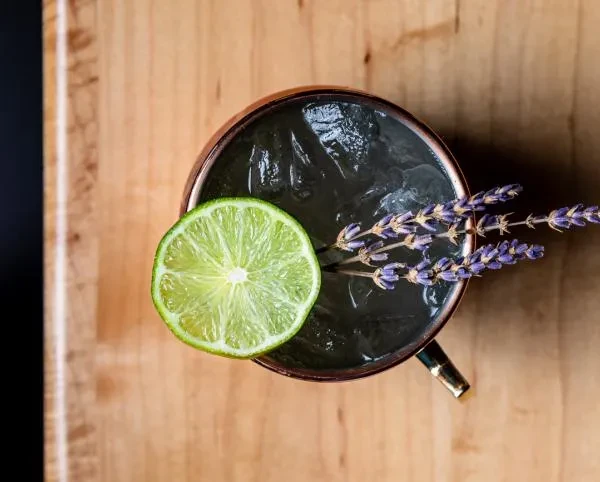 Dark cocktail in copper mug with ice, lime, and lavender.