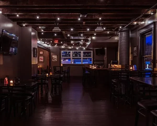Dimly lit restaurant interior, exposed beams, string lights, bar, and tables.