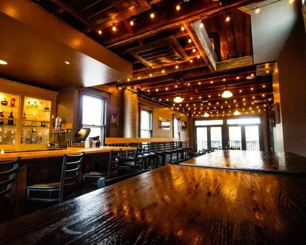 Rustic bar interior with dark wood, exposed beams, string lights.