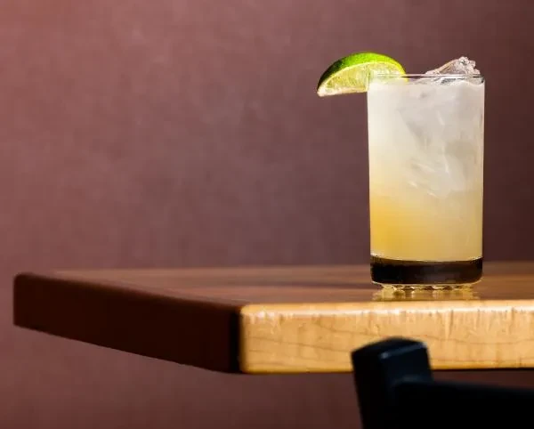 Layered drink with ice and lime wedge on a wooden surface.