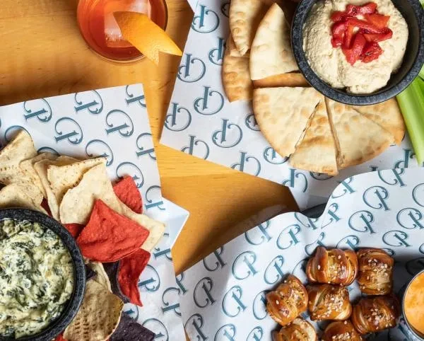 Flat-lay: Hummus, cocktail, spinach dip with chips, and pretzel bites.