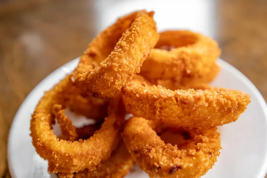 Close-up of golden-brown crispy onion rings piled on a white plate.