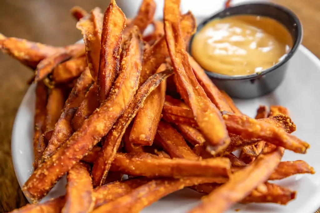 Crispy sweet potato fries on a white plate with dipping sauce.