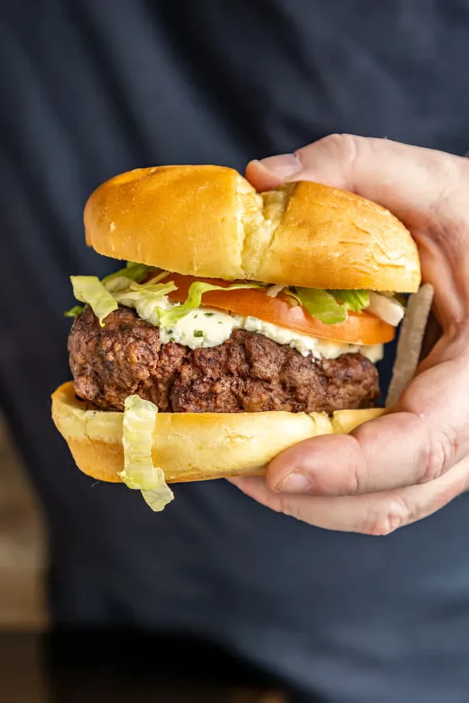 Hands hold a gourmet hamburger with beef patty, lettuce, tomato, sauce.