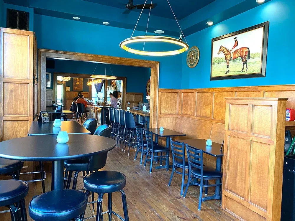 Teal restaurant interior with wooden wainscoting, black tables, and a bar.