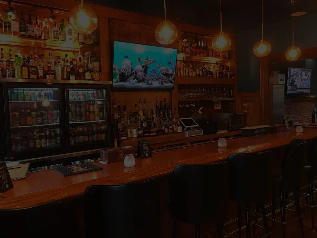 Dimly lit bar with backlit liquor shelves, counter, and stools.