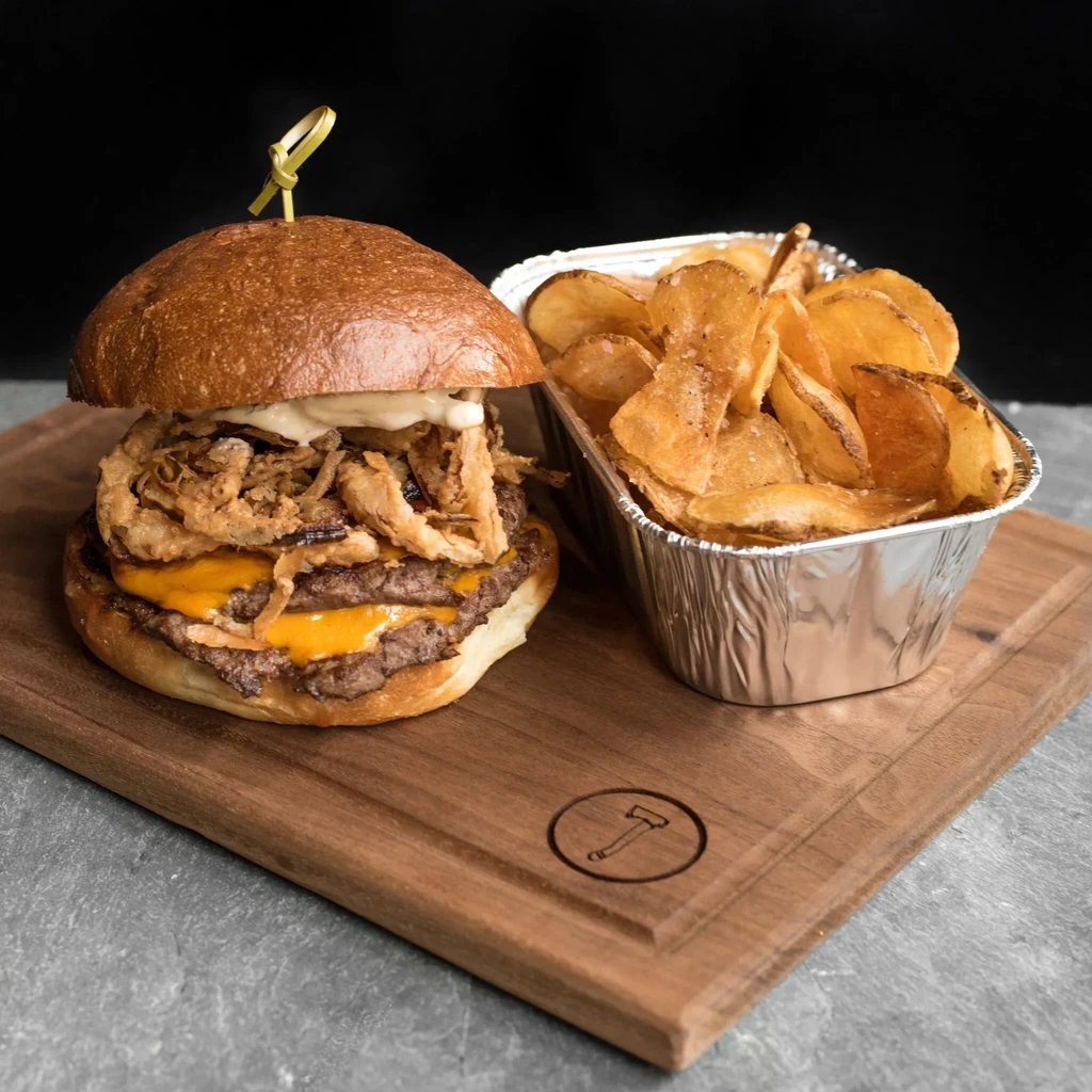 Stacked double cheeseburger with chips on a rustic wooden board.