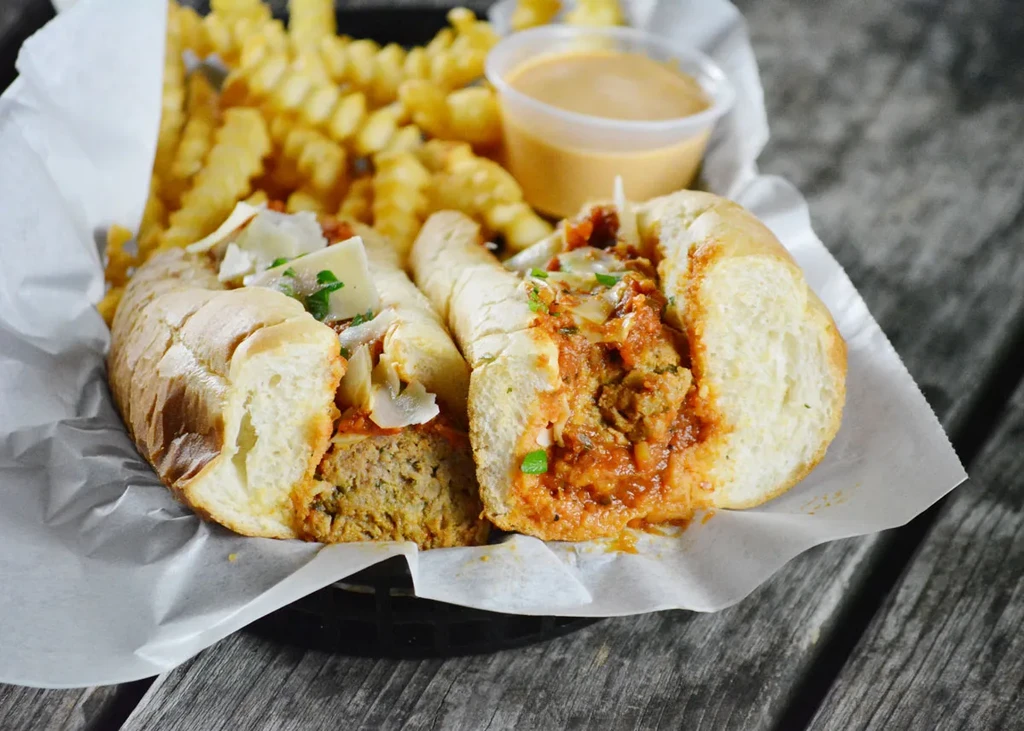 Halved meatball sandwich, crinkle fries, and dipping sauce in a basket.