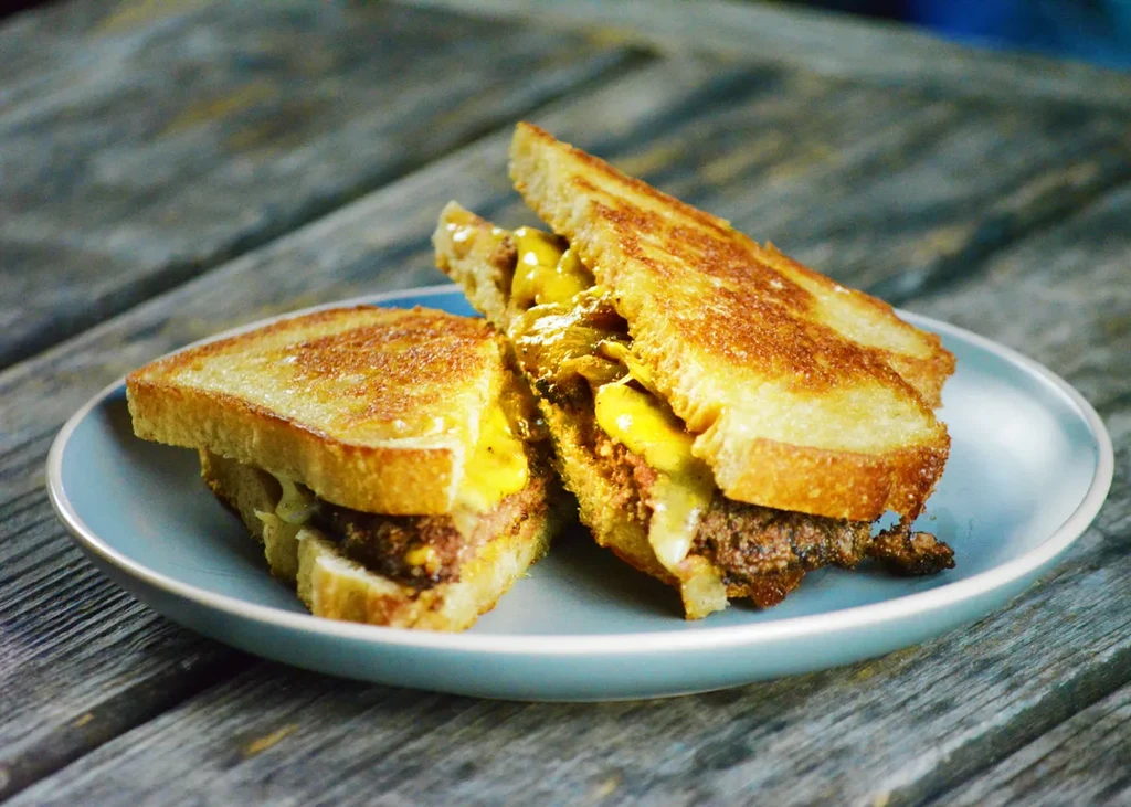 Grilled patty melt, cut in half, on a light blue plate.