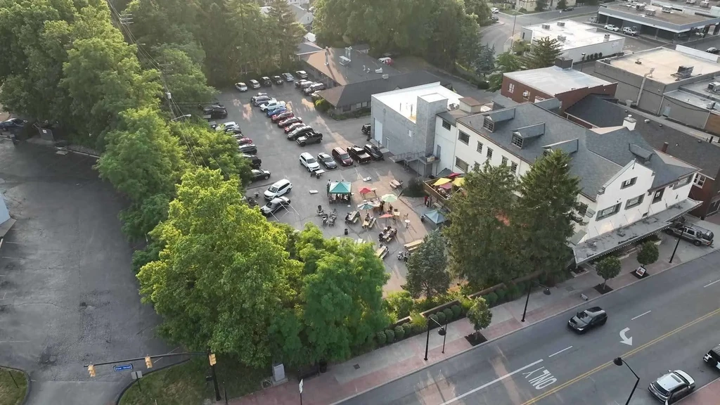 Aerial view: Outdoor gathering with people, colorful umbrellas, and many parked cars.