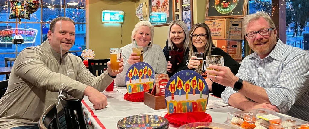 Birthday celebration with five smiling adults holding drinks in a restaurant.
