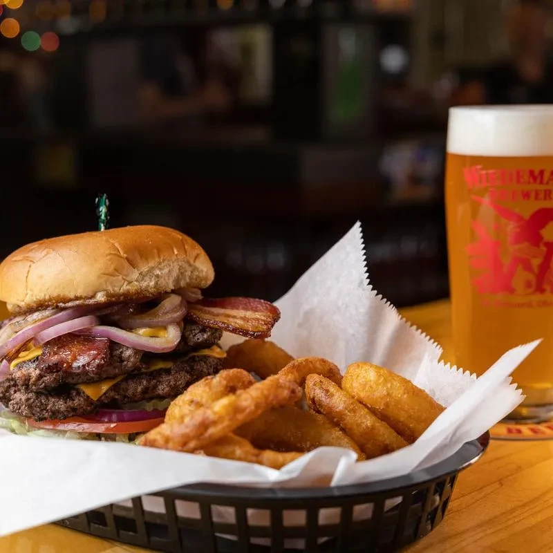 Close-up of a double-patty cheeseburger, fries, and Wiedeman Brewery beer.