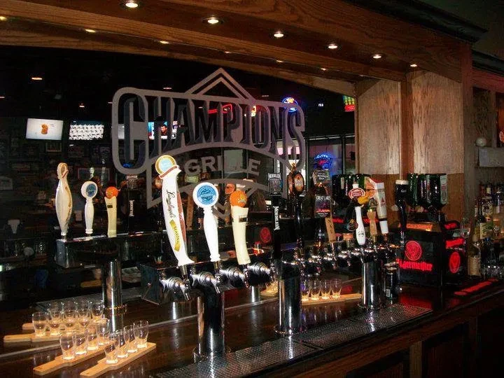 A wooden bar counter with beer taps, liquor, and "CHAMPIONS GRILLE" sign.