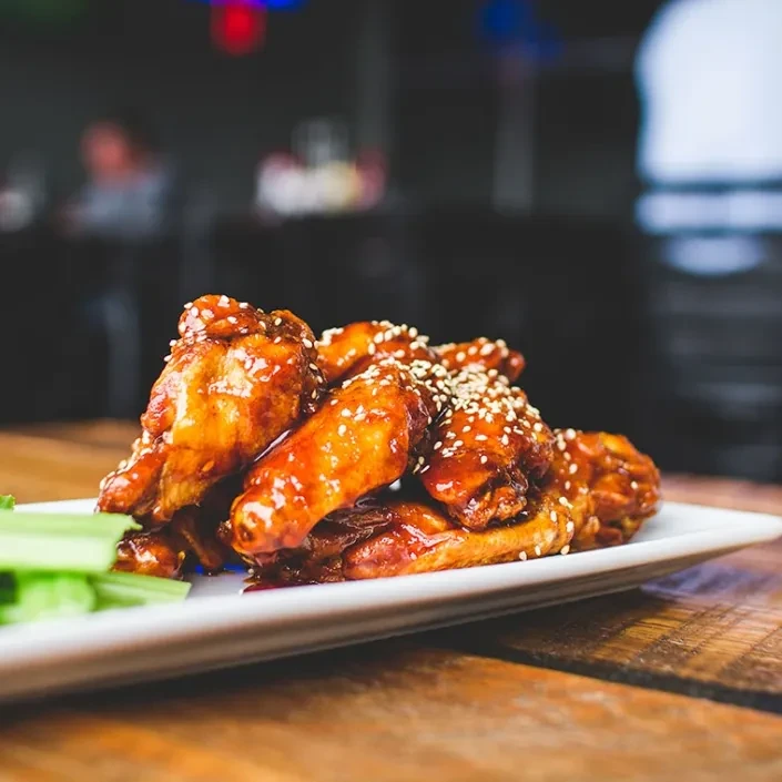 Plate of glazed chicken wings with sesame seeds and celery on a wooden table.