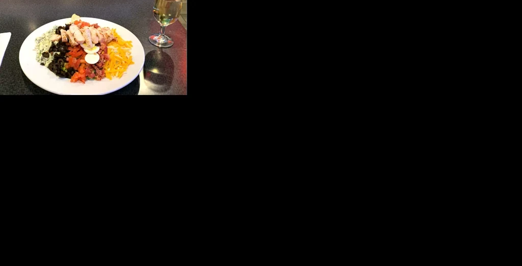Colorful chicken salad with egg and white wine on a dark table.