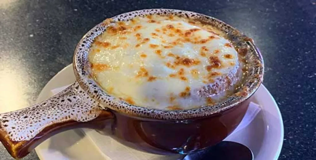 French onion soup in a speckled brown crock with bubbly melted cheese.