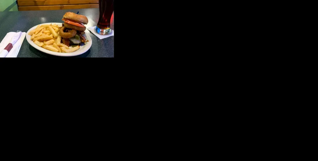 Plate of burger with onion rings, tomato, fries, and a drink.